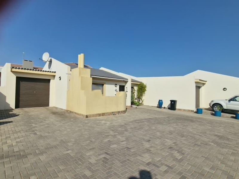 Front exterior view of the townhouse featuring a paved driveway, single garage, and boundary wall.