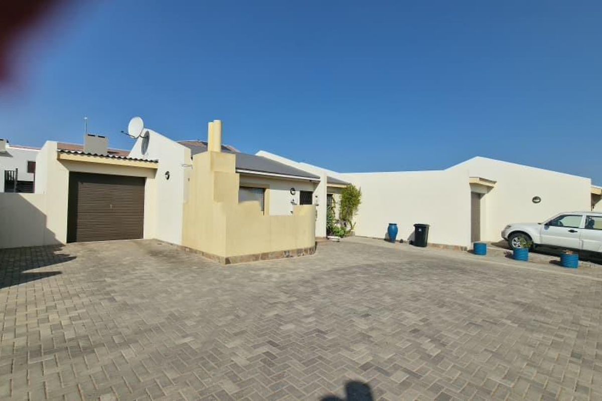 Front exterior view of the townhouse featuring a paved driveway, single garage, and boundary wall.