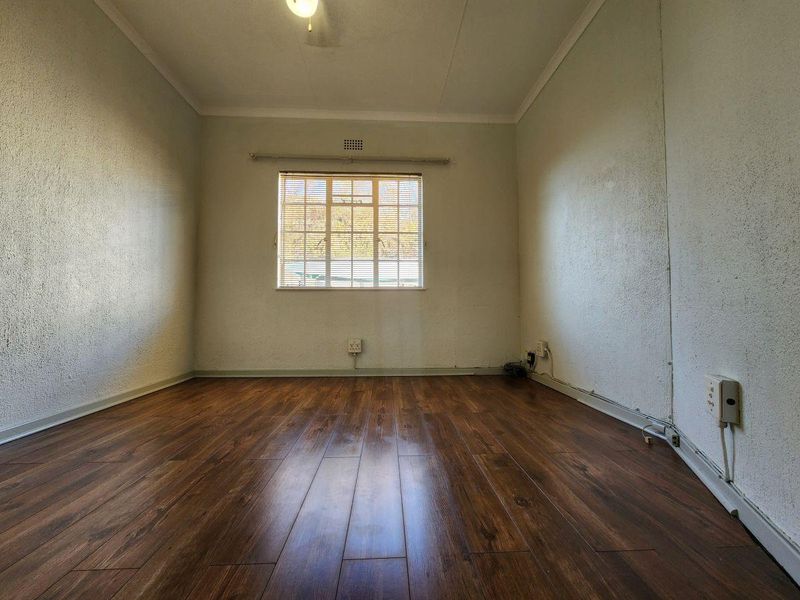An empty bedroom featuring dark laminate flooring, a central window with blinds, and visible surface-mounted electrical wiring.