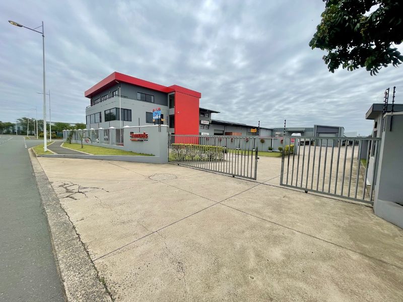 Front view of an industrial property featuring a multi-story office building, secure gated entrance with electric fencing, and a concrete driveway.