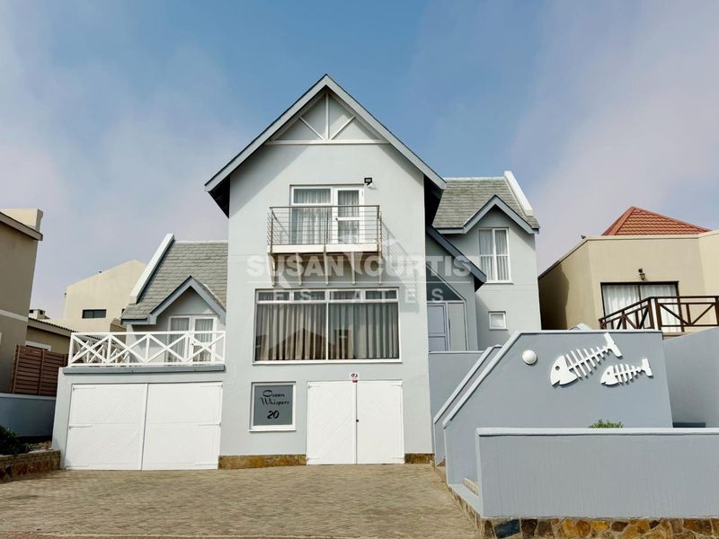 Front elevation of a multi-level coastal house featuring a paved driveway, double garage, and a balcony with metal railings.