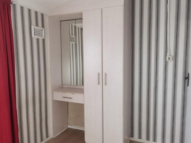 A bedroom featuring a built-in wardrobe with an integrated vanity unit, finished with striped wallpaper and wood-look flooring.