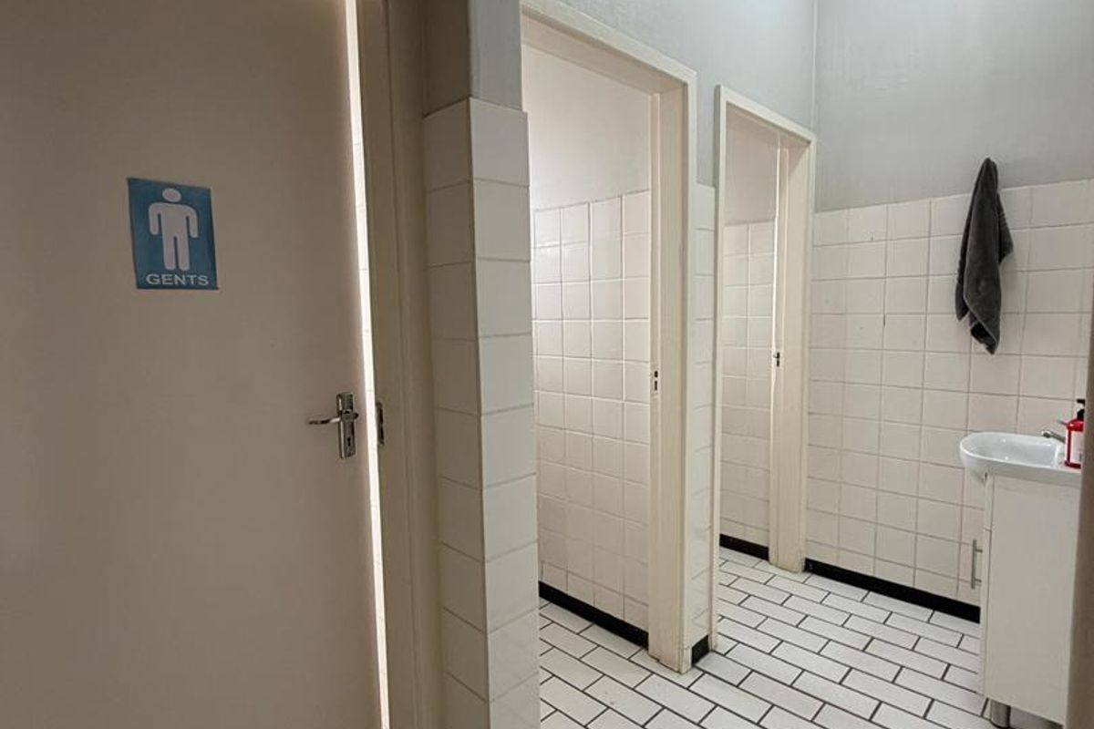 Functional office restroom facility featuring tiled walls and flooring, pedestal sink, and separate cubicle access.