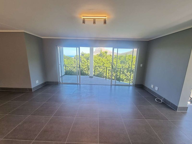 Spacious, empty living area featuring large sliding glass doors that open onto a balcony with scenic views and modern tiled flooring.