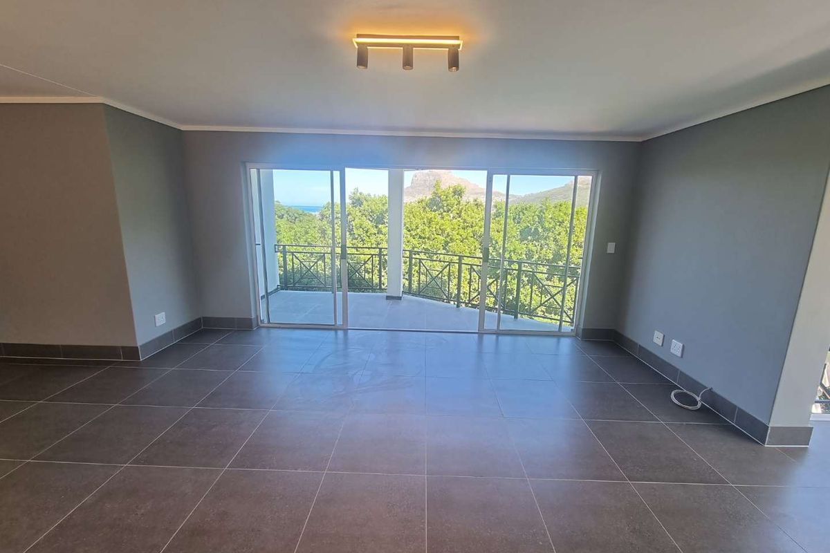 Spacious, empty living area featuring large sliding glass doors that open onto a balcony with scenic views and modern tiled flooring.