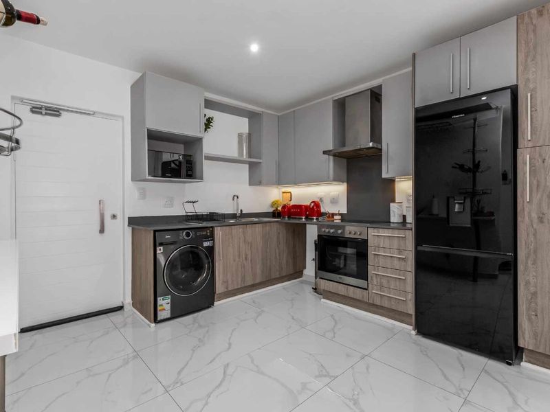Modern kitchen featuring sleek two-tone cabinetry, stone countertops, integrated appliances, and high-gloss marble-look floor tiles.