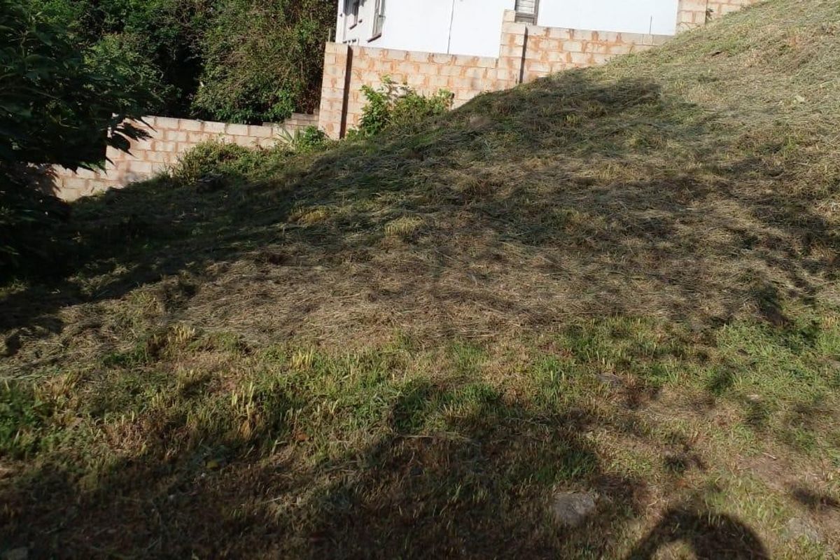 A sloped residential plot featuring a retaining wall and cleared vegetation, offering potential for landscaping or terraced garden development.