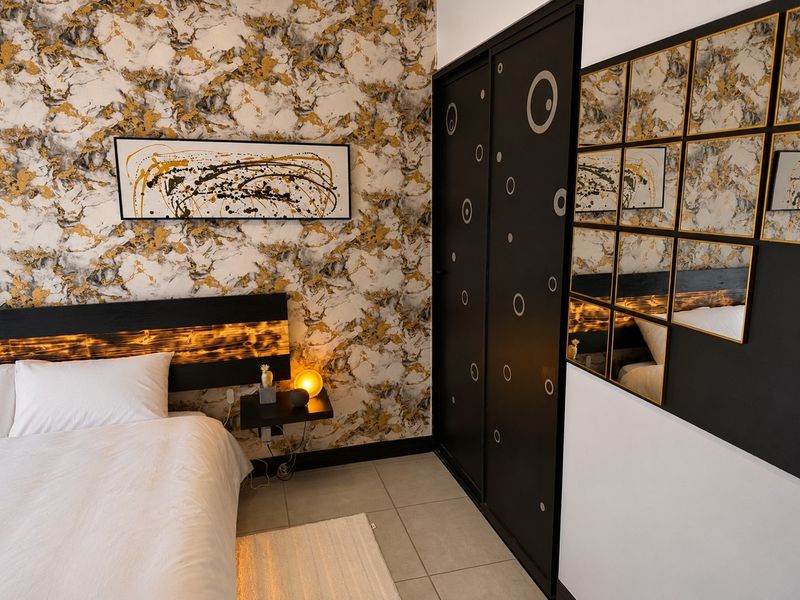 A modern bedroom featuring bold marble-patterned wallpaper, tiled flooring, and a sleek black built-in wardrobe with decorative circular accents.