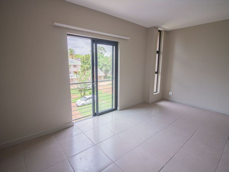 A bright, empty bedroom featuring neutral tiled flooring, a sliding glass door leading to a balcony, and a tall vertical window.