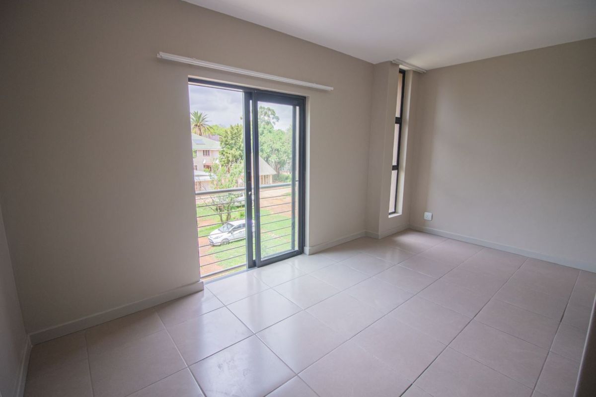 A bright, empty bedroom featuring neutral tiled flooring, a sliding glass door leading to a balcony, and a tall vertical window.