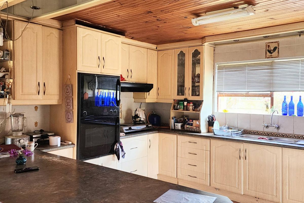 A functional kitchen featuring light-toned cabinetry, a built-in oven, a double sink, and a distinctive timber-paneled ceiling.