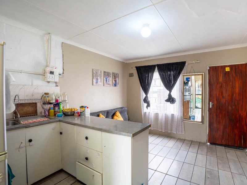 Open plan kitchen and living area featuring tiled flooring, functional cabinetry, and direct access to the exterior via a timber door.