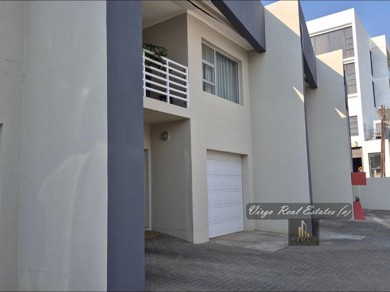 Front elevation of a modern townhouse featuring a paved driveway, integrated garage, and an upper-level balcony with clean architectural lines.