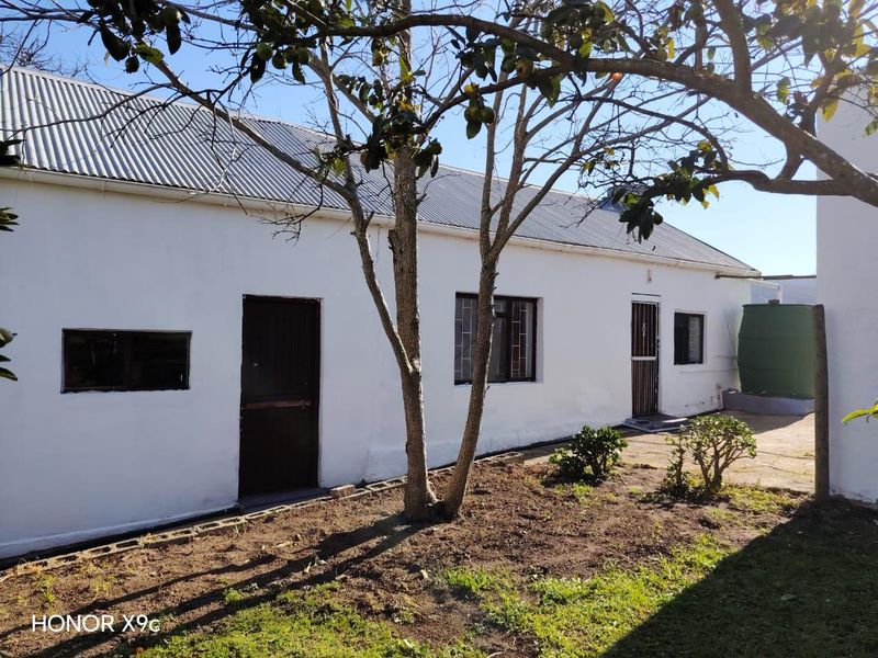 Rear exterior view of the property featuring a corrugated metal roof, security gates, and a paved patio area with an adjacent water tank.