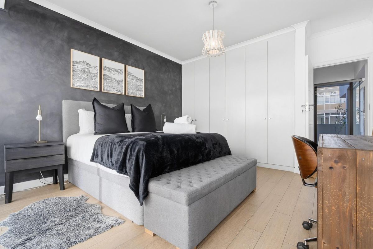 A well-presented bedroom featuring modern laminate flooring, extensive built-in cupboards, and a striking dark feature wall.