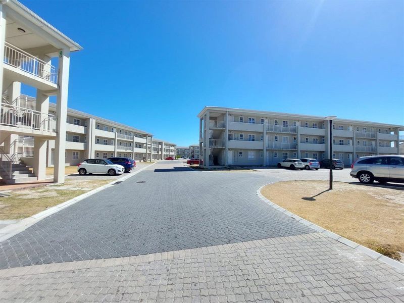 A view of the apartment complex exterior featuring paved driveways, multi-story residential blocks with balconies, and external staircases under a clear blue sky.