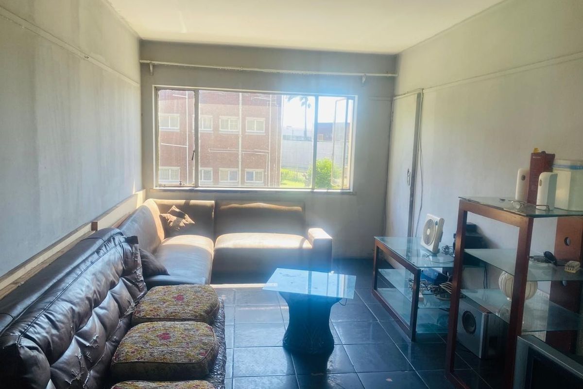 A living room featuring tiled flooring and a large window, providing natural light. The space requires cosmetic updates to the wall finishes.