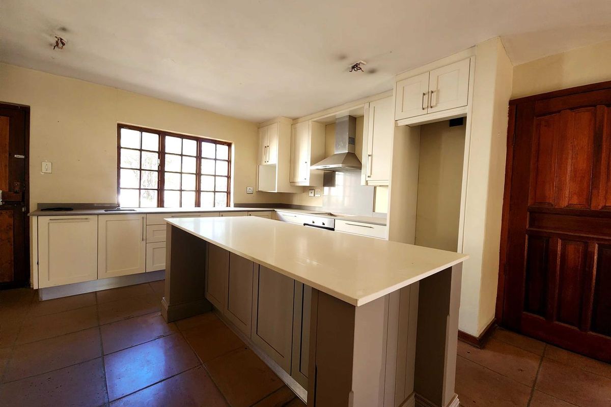 A spacious kitchen featuring a central island, built-in cabinetry, stainless steel extractor fan, and tiled flooring, offering a functional layout for culinary activities.