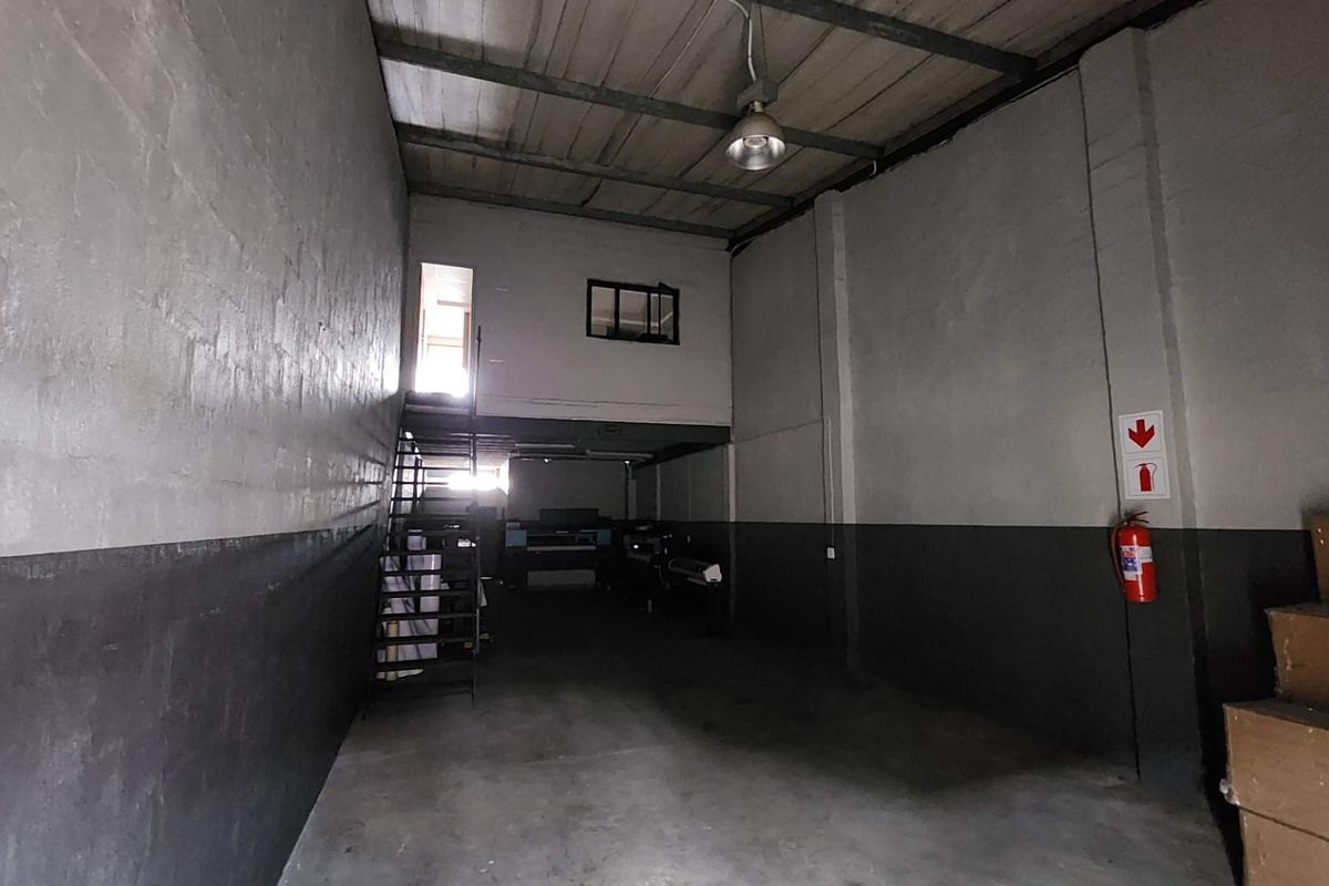 Spacious industrial utility area featuring a mezzanine level, metal staircase, and high ceilings, suitable for storage or workshop operations.