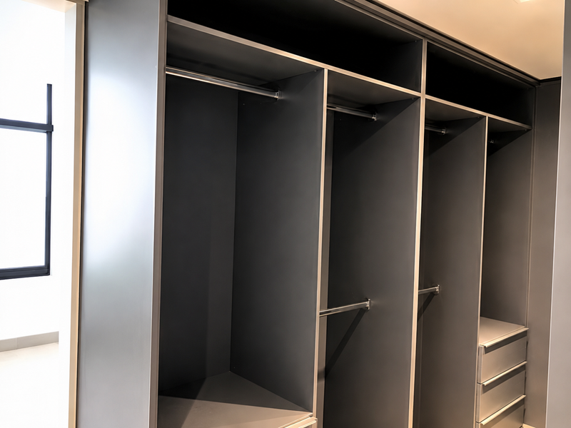 A modern, empty bedroom featuring a large, dark-toned built-in wardrobe with integrated hanging rails and storage drawers.