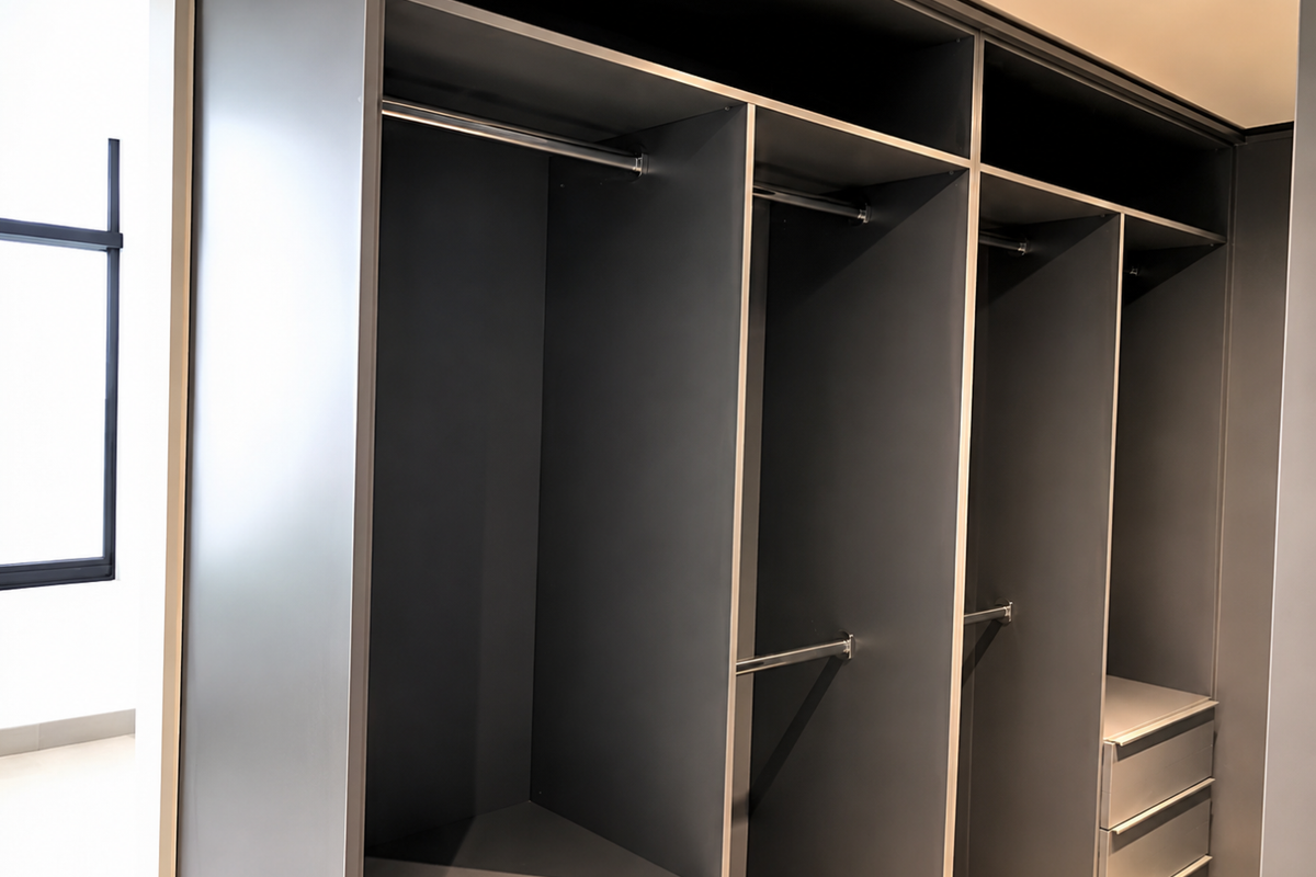 A modern, empty bedroom featuring a large, dark-toned built-in wardrobe with integrated hanging rails and storage drawers.