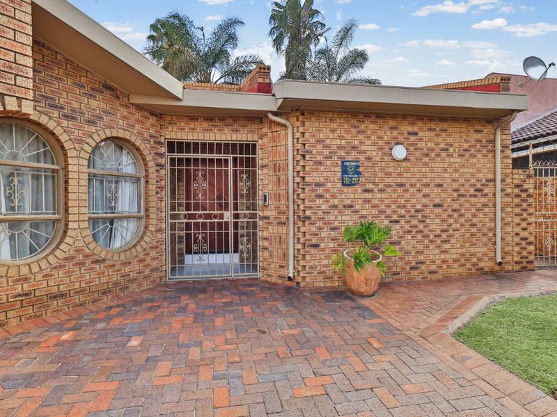 Front entrance of a face brick house featuring a paved driveway, secure metal gate, and distinctive arched windows.