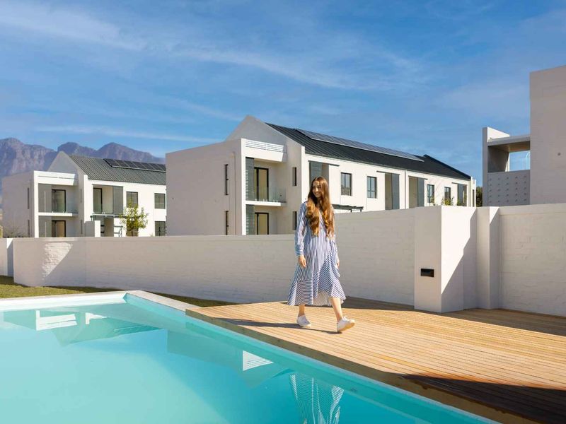 Modern apartment complex featuring a pristine swimming pool with timber decking and mountain views in the background.