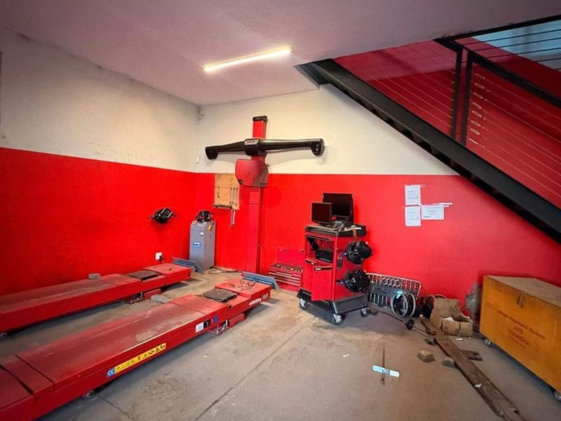 Industrial garage space featuring a built-in vehicle lift, concrete flooring, and a metal staircase leading to an upper level.