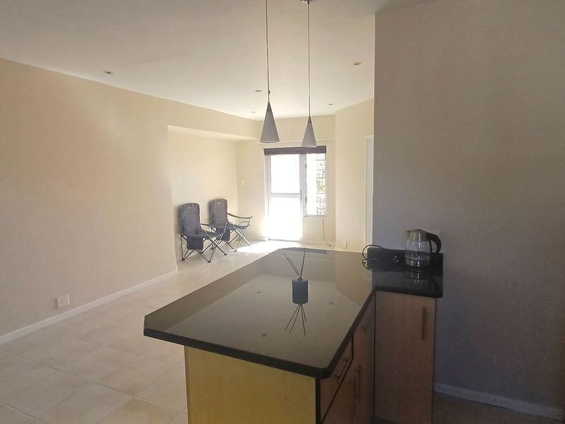 Open-plan living area featuring a kitchen island with granite countertops, tiled flooring, and recessed lighting, leading to a bright living space.