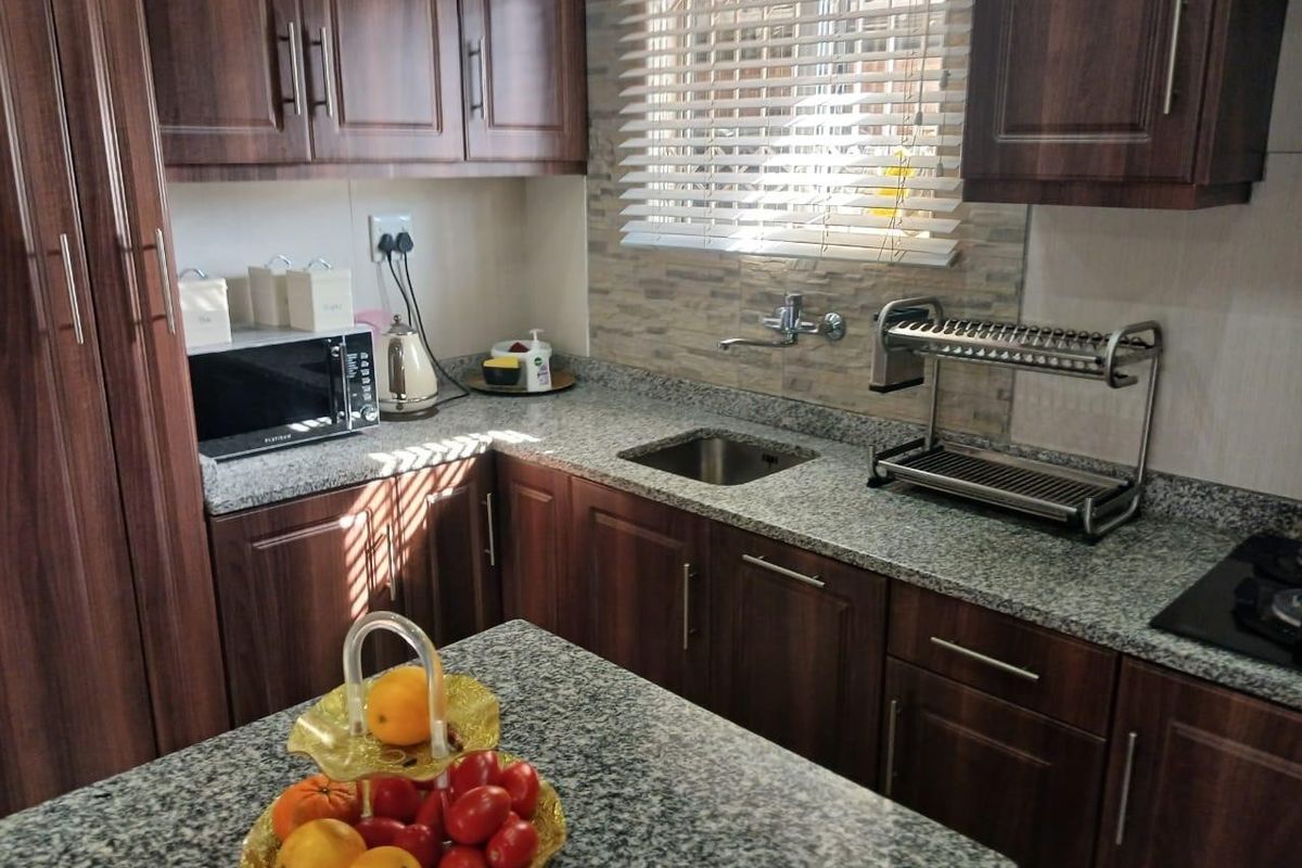 A functional kitchen featuring dark wood cabinetry, granite countertops, a stainless steel sink, and a built-in hob with a stone tile splashback.