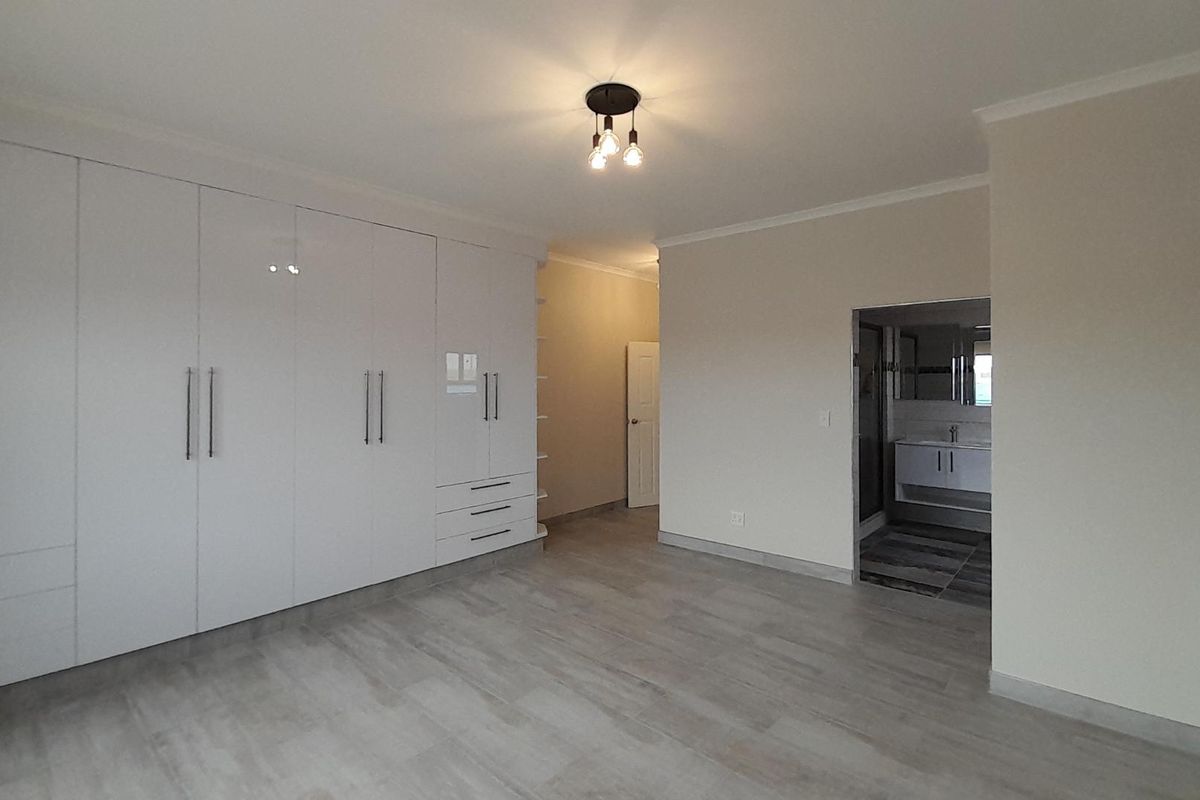 Spacious bedroom featuring extensive white built-in cupboards, modern light-toned laminate flooring, and direct access to an en-suite bathroom.