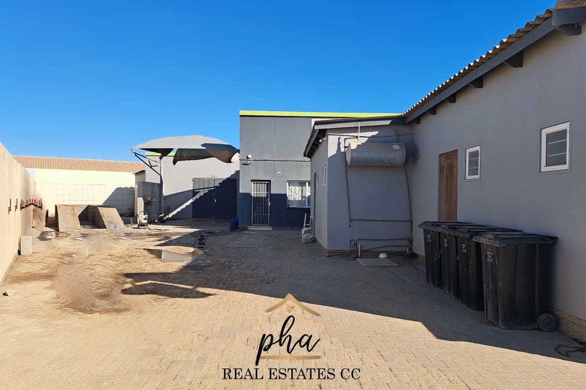 Rear exterior view of the business property featuring paved yard space, external water heating unit, and access doors to the building structure.