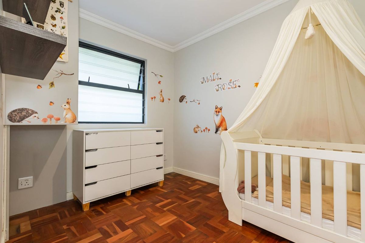 A well-maintained bedroom featuring classic parquet flooring, neutral wall finishes, and a window providing natural light.