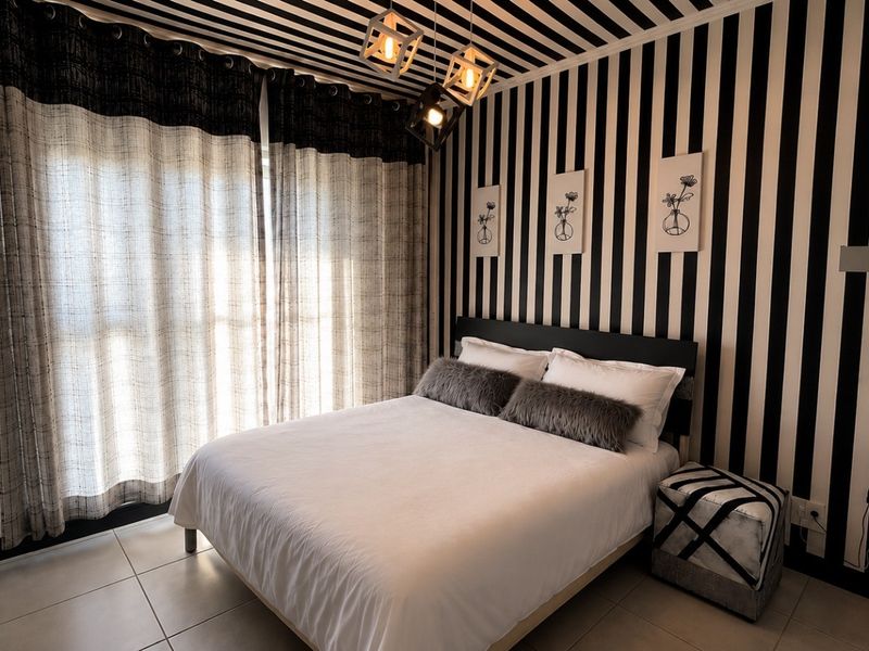 A bedroom featuring tiled flooring and modern geometric pendant lighting, characterized by bold striped wall and ceiling treatments.