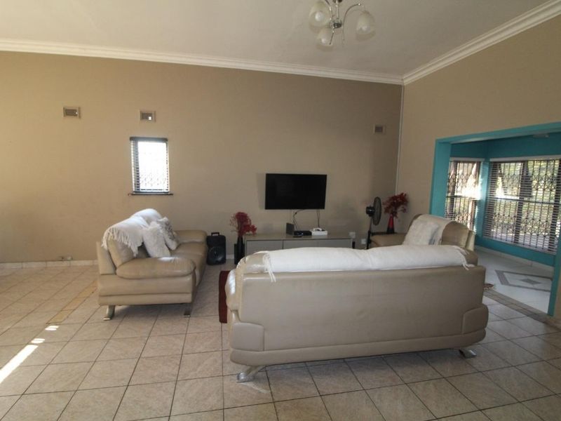 Spacious living room featuring neutral wall tones, tiled flooring, and security bars on windows, offering a functional layout for comfortable family living.