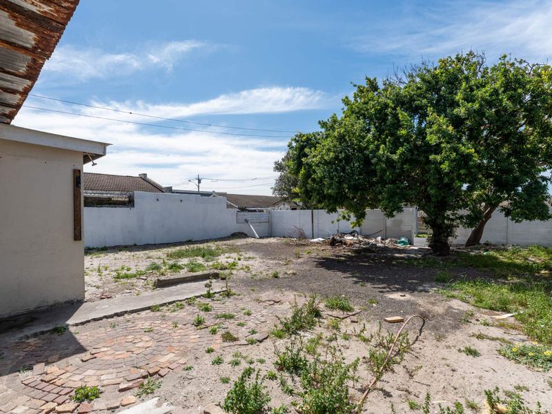 A spacious rear garden area featuring a paved patio, mature tree, and precast boundary walls, offering significant potential for landscaping and outdoor improvement.