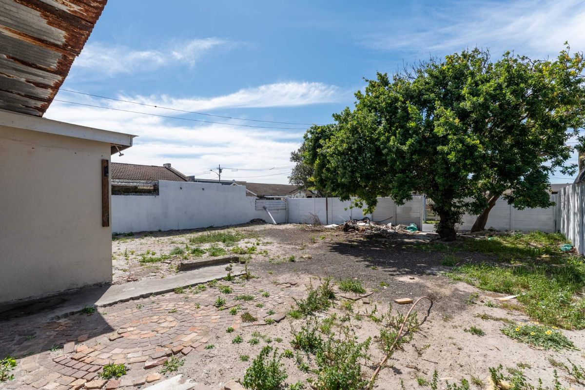 A spacious rear garden area featuring a paved patio, mature tree, and precast boundary walls, offering significant potential for landscaping and outdoor improvement.