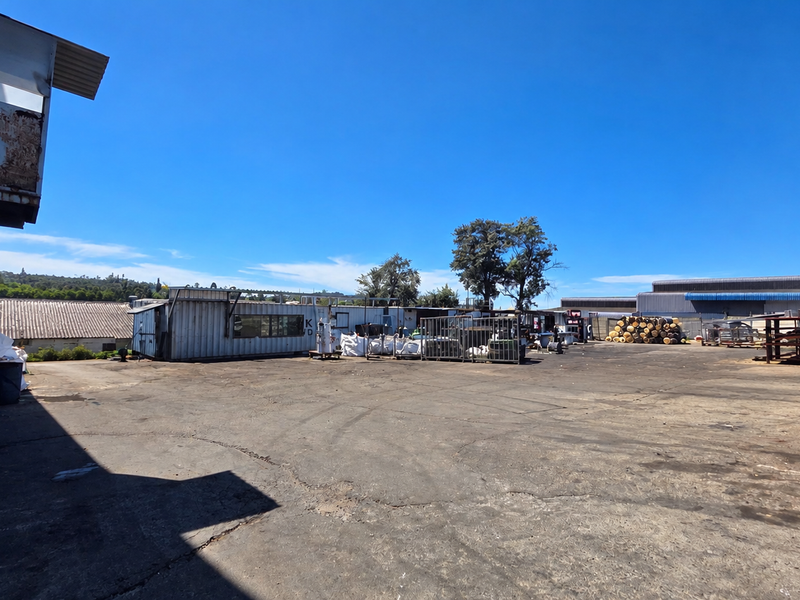 Expansive industrial yard featuring asphalt paving, metal storage structures, and perimeter security fencing, suitable for logistics or manufacturing operations.