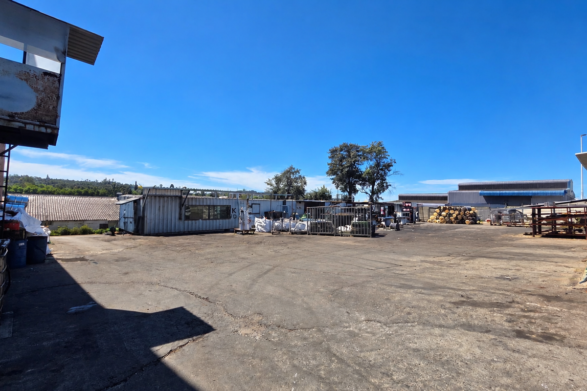 Expansive industrial yard featuring asphalt paving, metal storage structures, and perimeter security fencing, suitable for logistics or manufacturing operations.