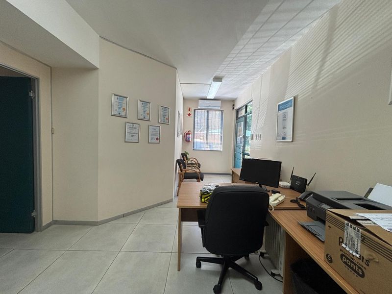 A functional office space featuring tiled flooring, wall-mounted air conditioning, and ample natural light through a window.