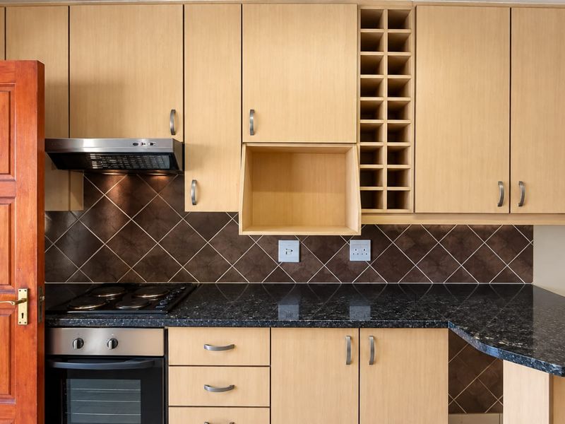 A well-maintained kitchen featuring light wood cabinetry, black granite countertops, a built-in oven with hob, and a decorative wine rack.
