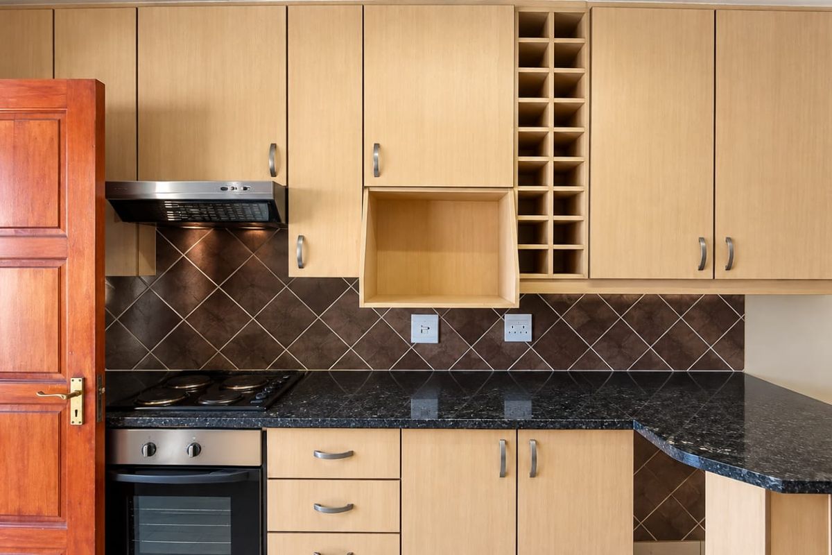 A well-maintained kitchen featuring light wood cabinetry, black granite countertops, a built-in oven with hob, and a decorative wine rack.