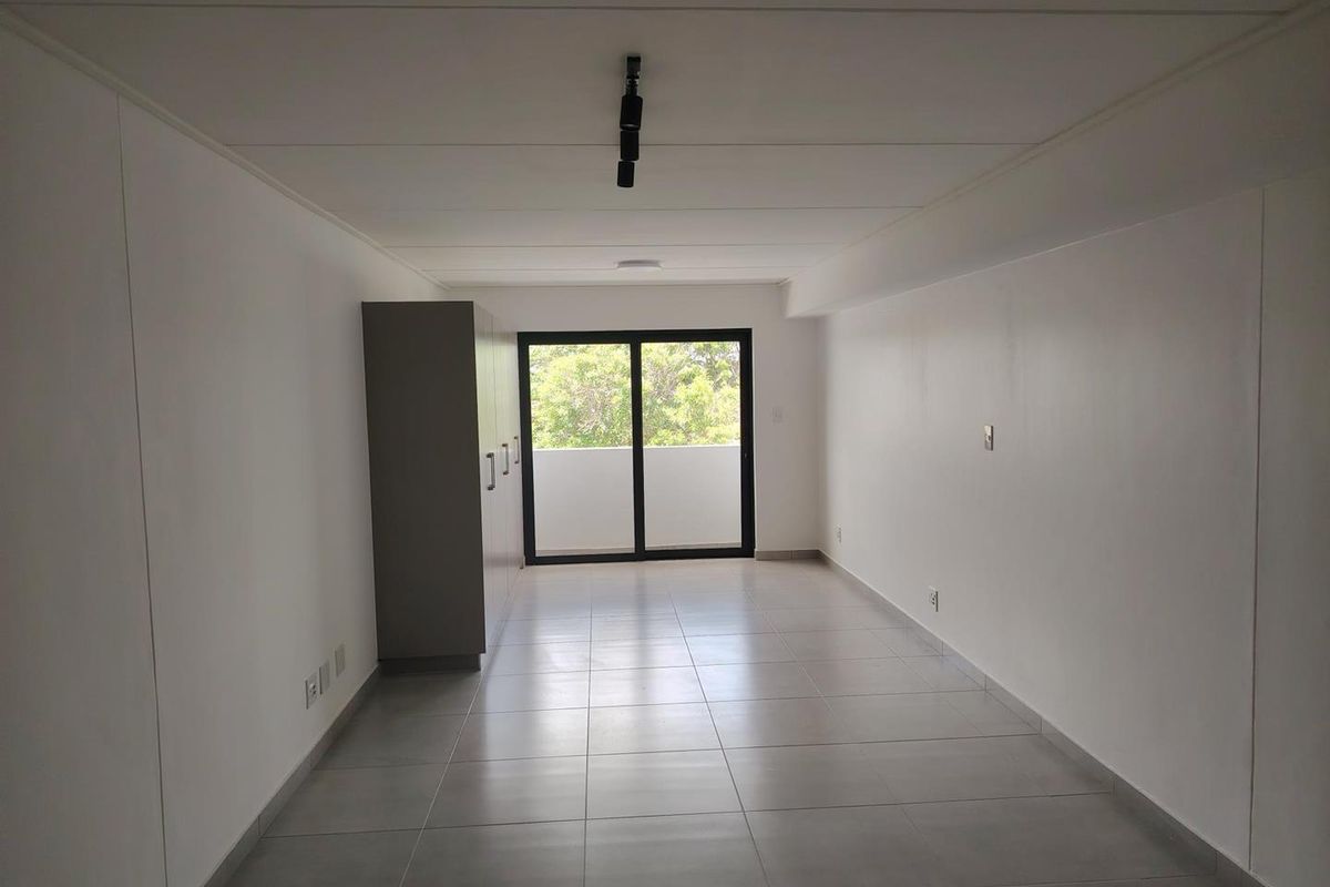 A bright, empty bedroom featuring neutral tiled flooring, built-in cupboards, and a sliding glass door leading to an outdoor balcony area.