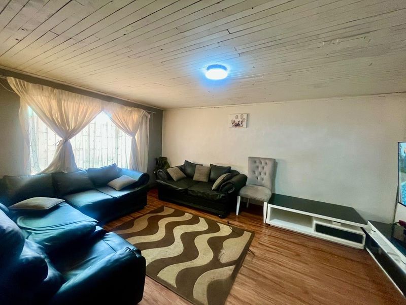 A living room featuring timber-look laminate flooring and a painted timber plank ceiling with security bars installed on the window.
