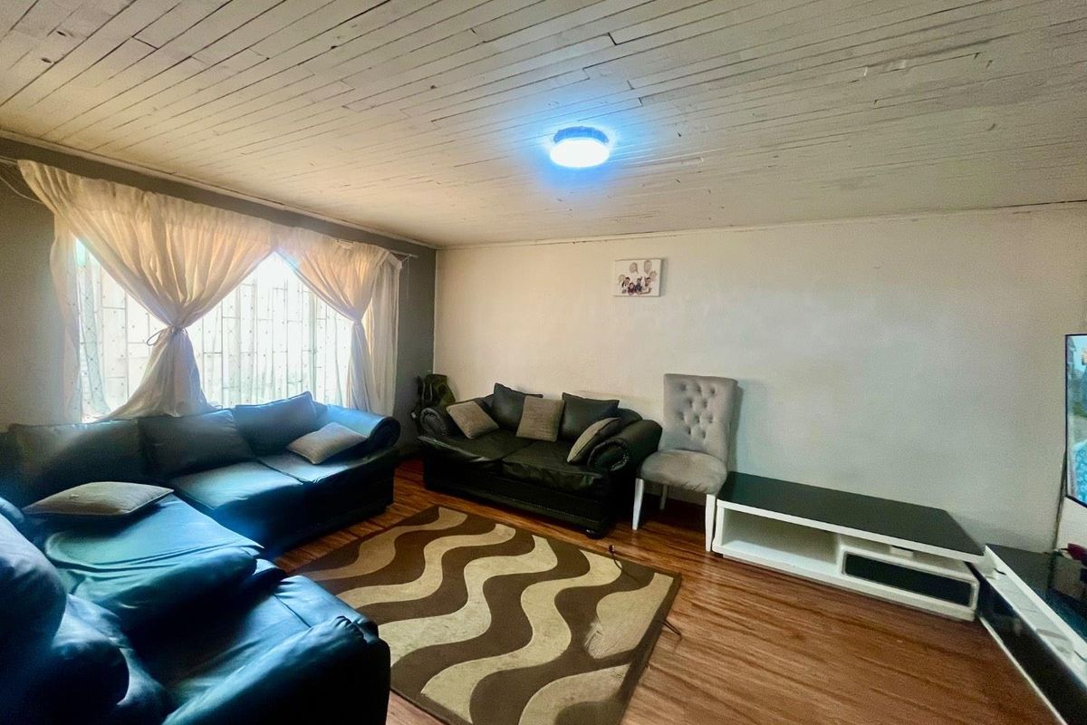A living room featuring timber-look laminate flooring and a painted timber plank ceiling with security bars installed on the window.