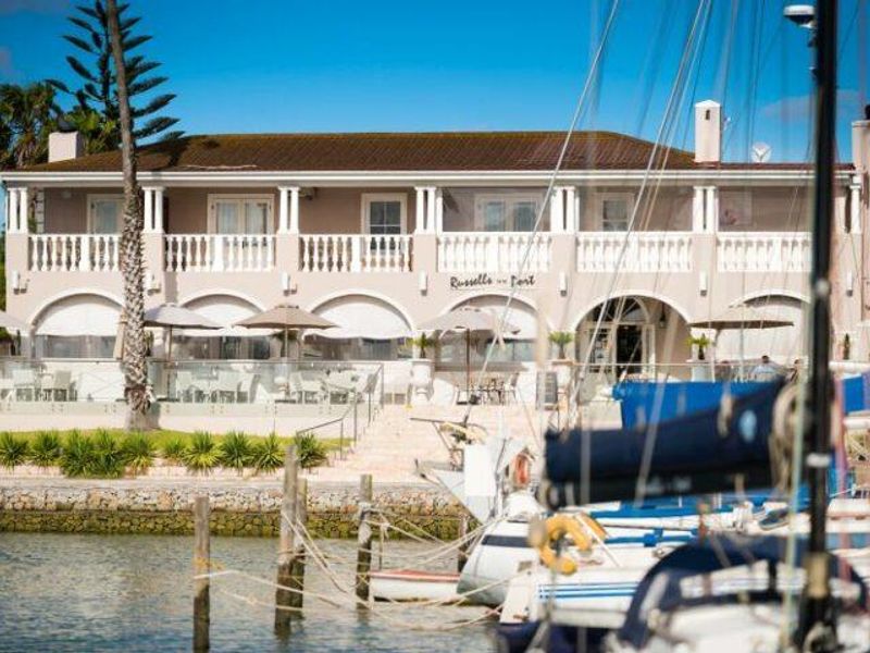 A view of the rear facade of the property featuring a covered patio, upper balcony with balustrades, and direct access to the waterfront.