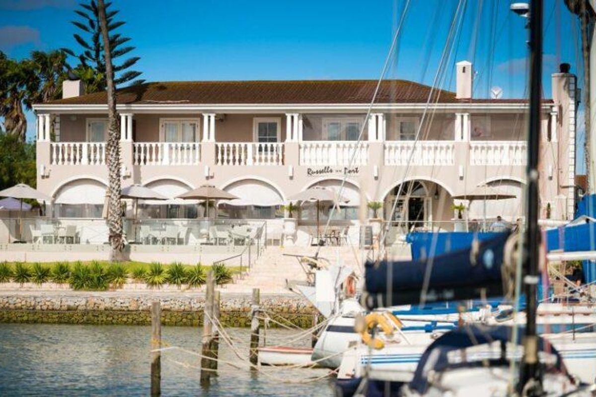 A view of the rear facade of the property featuring a covered patio, upper balcony with balustrades, and direct access to the waterfront.