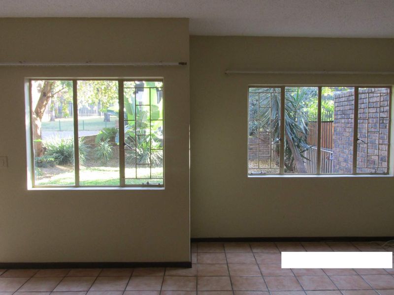 An empty living room featuring tiled flooring, large windows with security bars, and neutral wall tones, offering a blank canvas for interior design.
