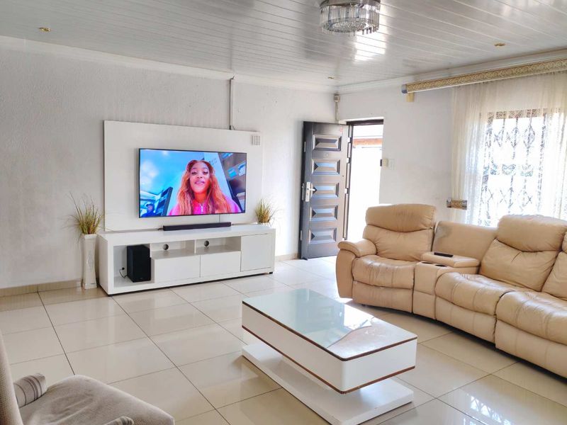 A bright living room featuring tiled flooring, a tongue and groove ceiling, and a built-in media wall unit with direct access to the exterior.