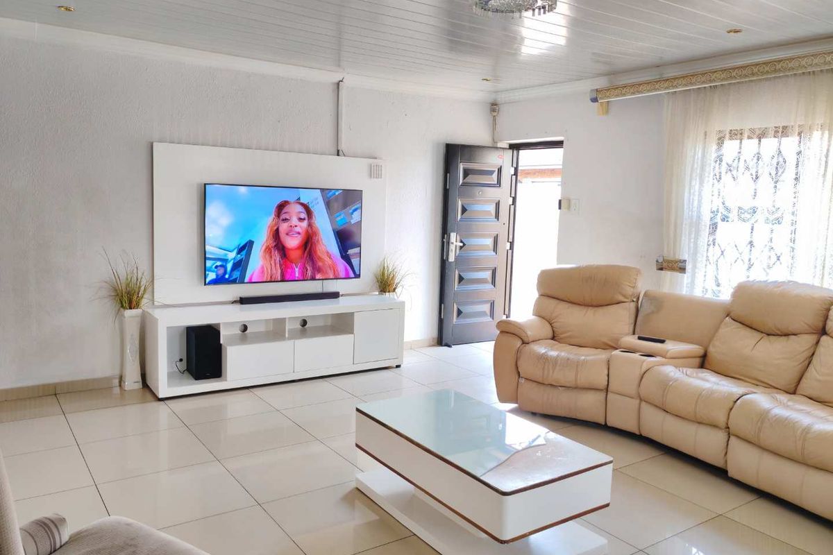 A bright living room featuring tiled flooring, a tongue and groove ceiling, and a built-in media wall unit with direct access to the exterior.